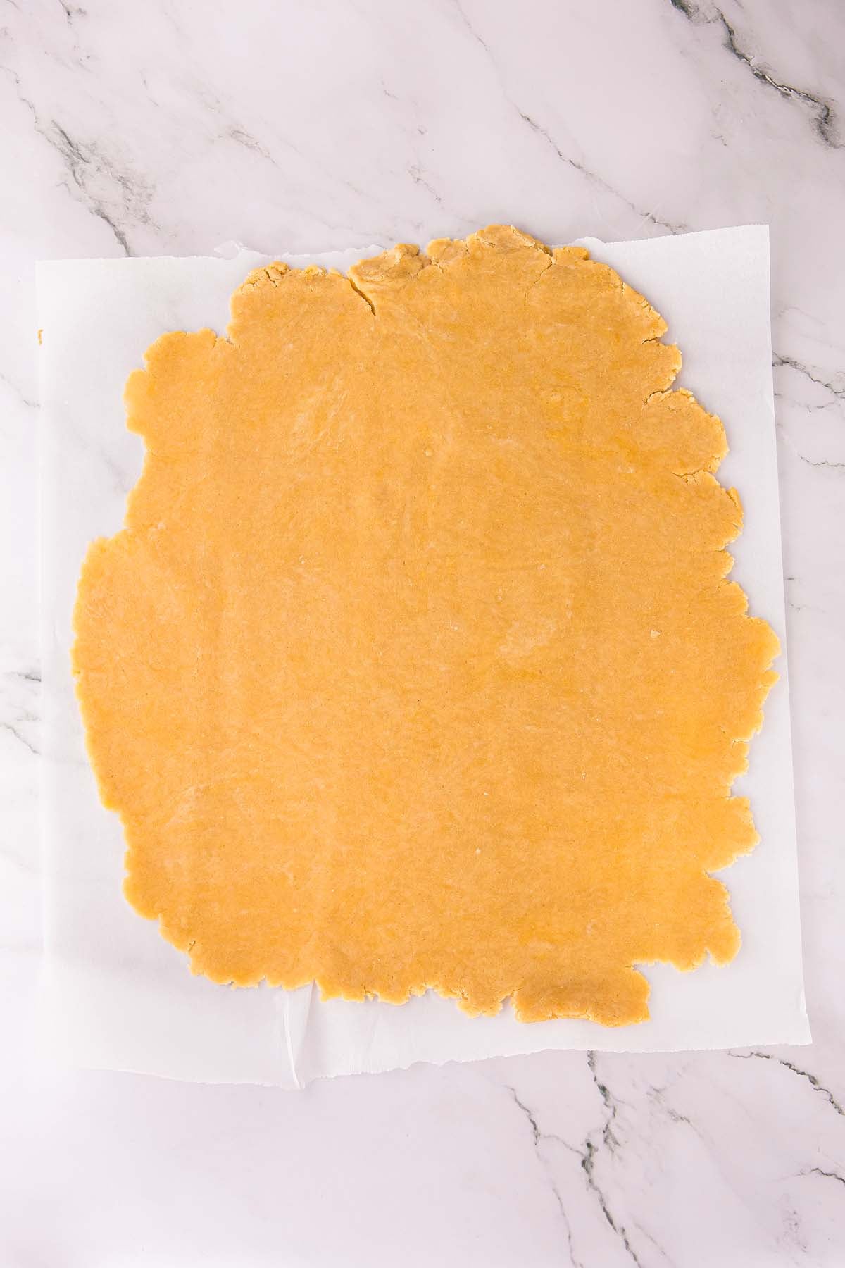 Rolled out dough on parchment paper, ready to be cut, on a white marble surface.