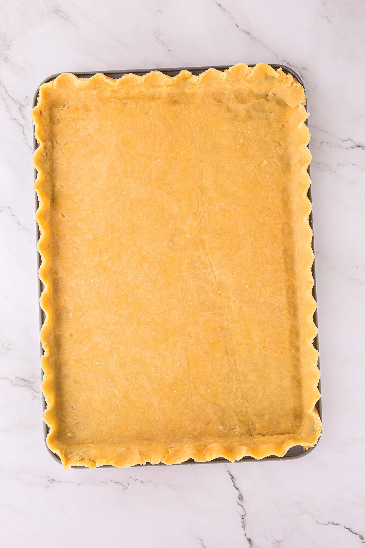 Rectangular baking pan filled with unbaked pie crust, edges crimped, on a marble surface.