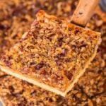 A close-up of a pecan slab pie piece being lifted from a pan with a metal spatula.