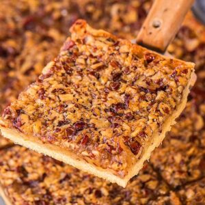 A close-up of a pecan slab pie piece being lifted from a pan with a metal spatula.
