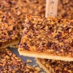 A spatula lifts a square pecan slab pie piece from a baking tray.