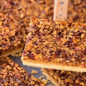 A spatula lifts a square pecan slab pie piece from a baking tray.