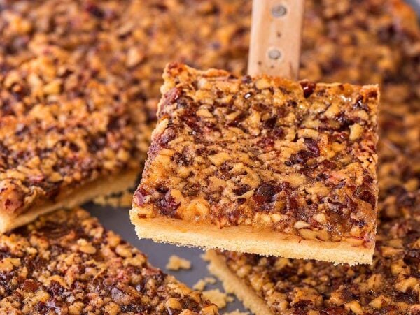 A spatula lifts a square pecan slab pie piece from a baking tray.