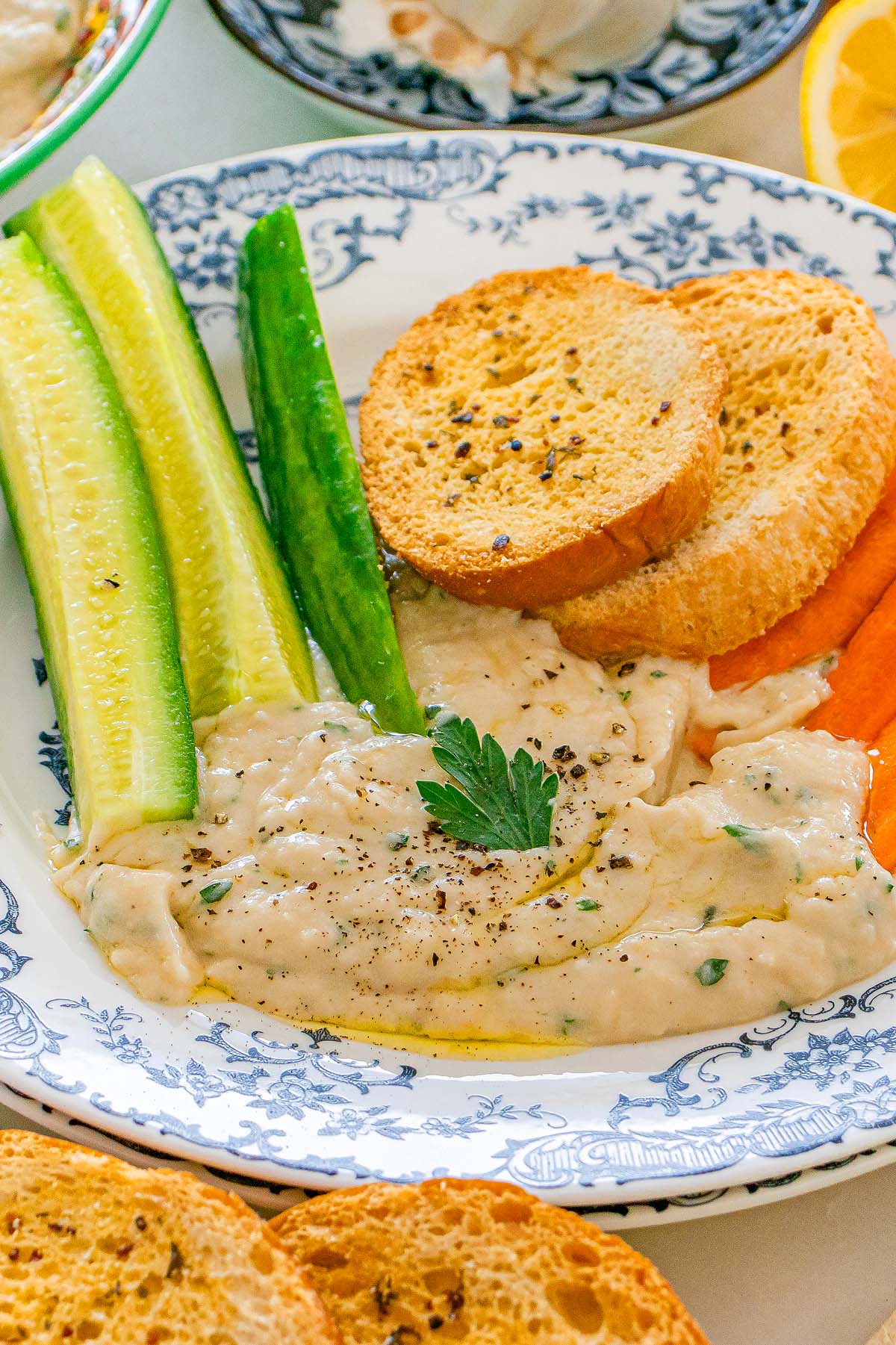Tuscan white bean dip garnished with parsley, served with cucumber sticks, carrot sticks, and toasted bread slices.