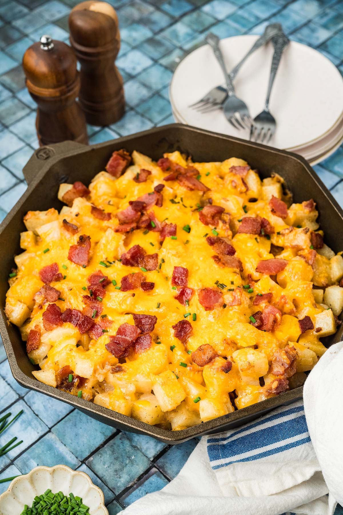 A cast iron skillet filled with potato bites topped with melted cheddar cheese, bacon, and chives.