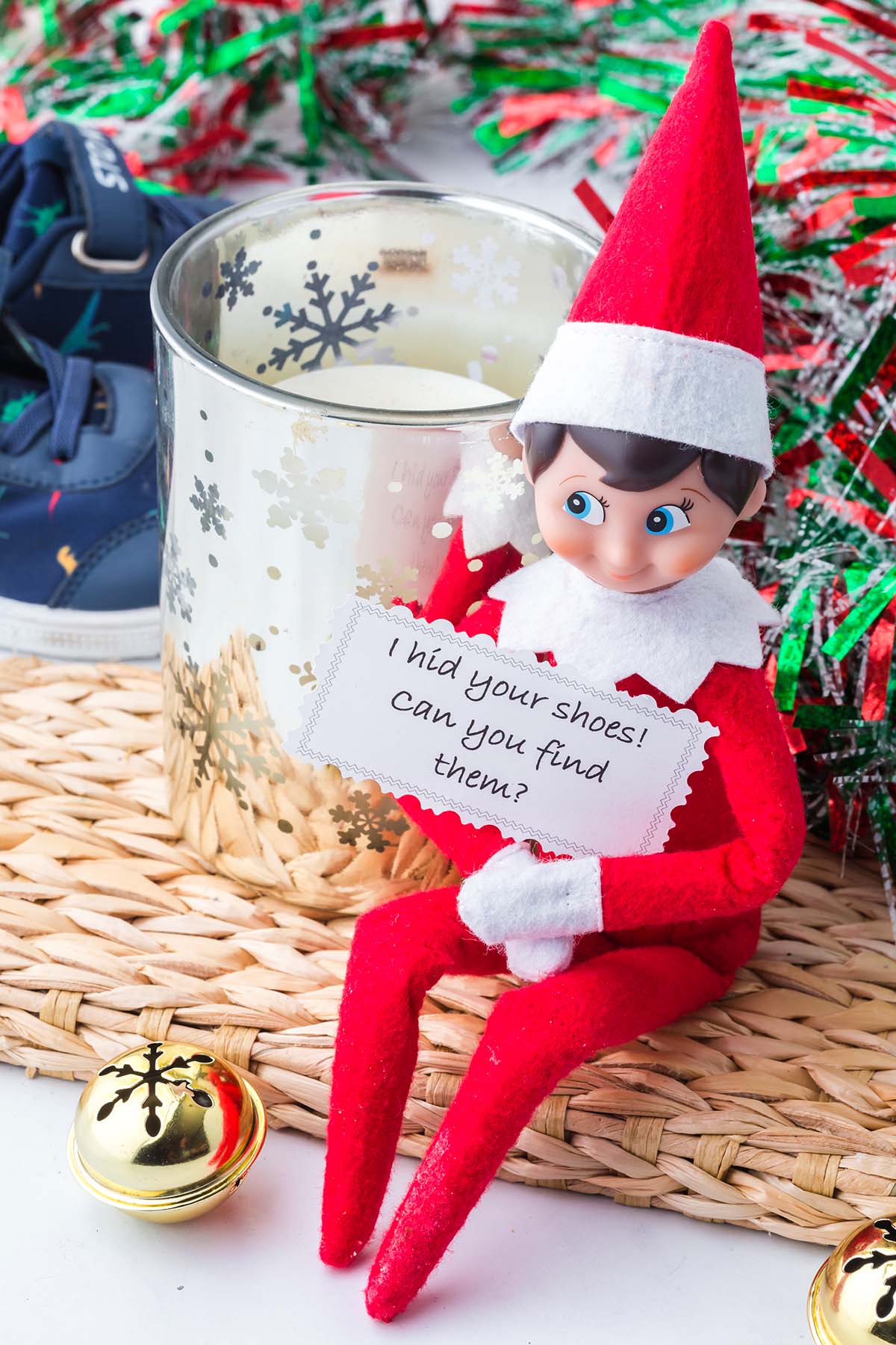 An Elf on the Shelf doll holds a note that reads, “I hid your shoes! can you find them?”.