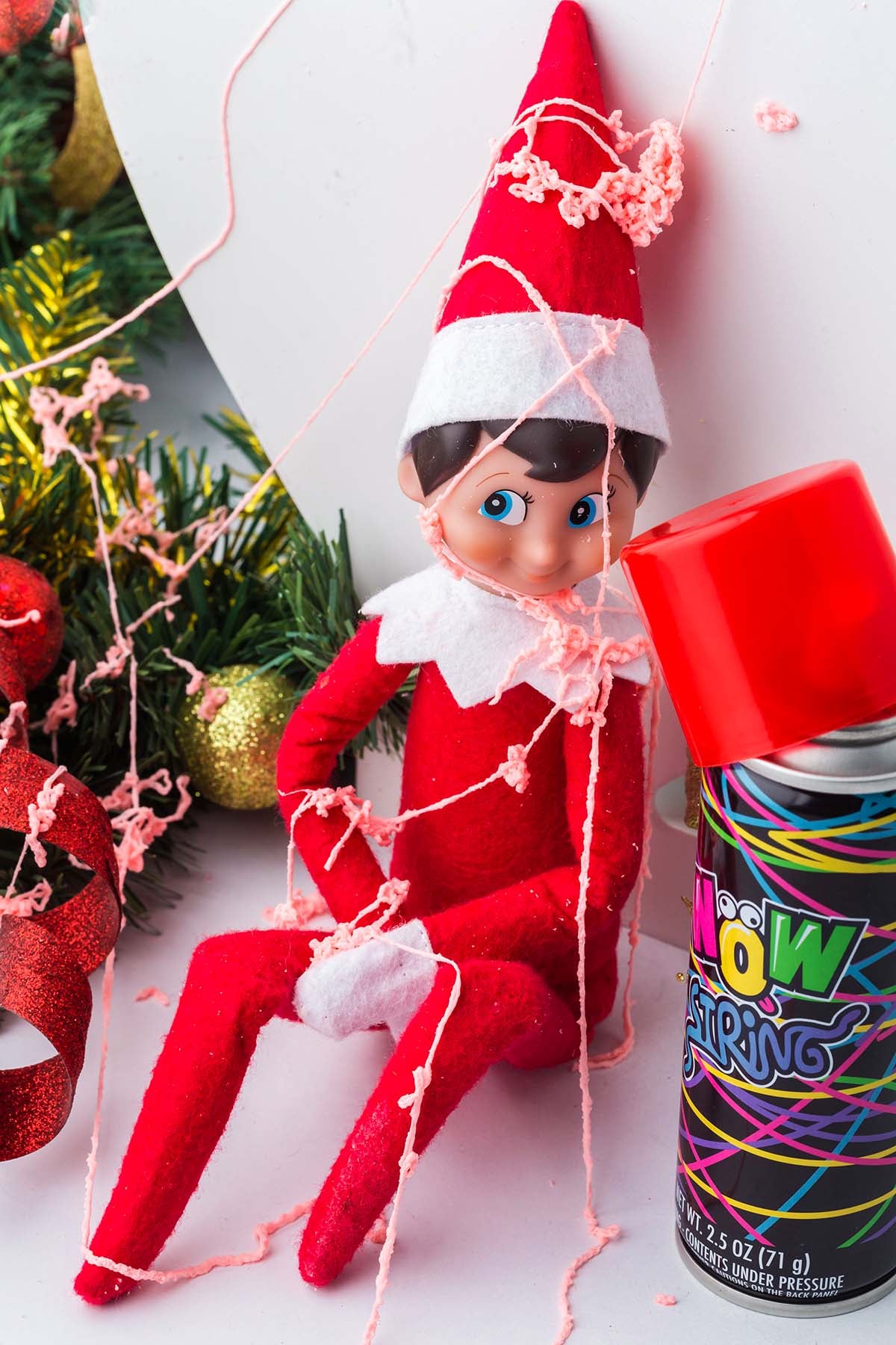 Elf on the Shelf doll covered in pink silly string next to a can of silly string.