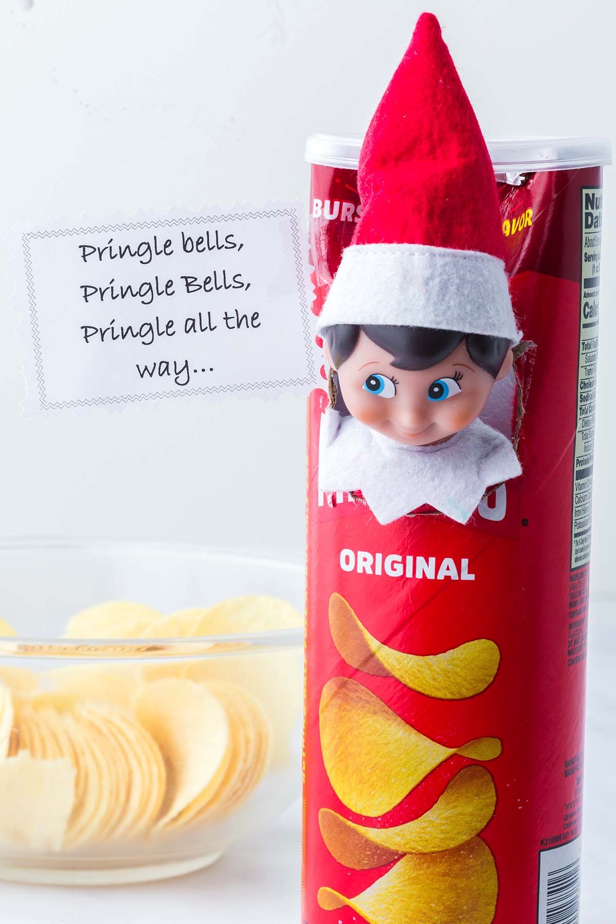 An elf doll peeking out of a Pringles can next to a note reading “Pringle bells, Pringle Bells, Pringle all the way...”