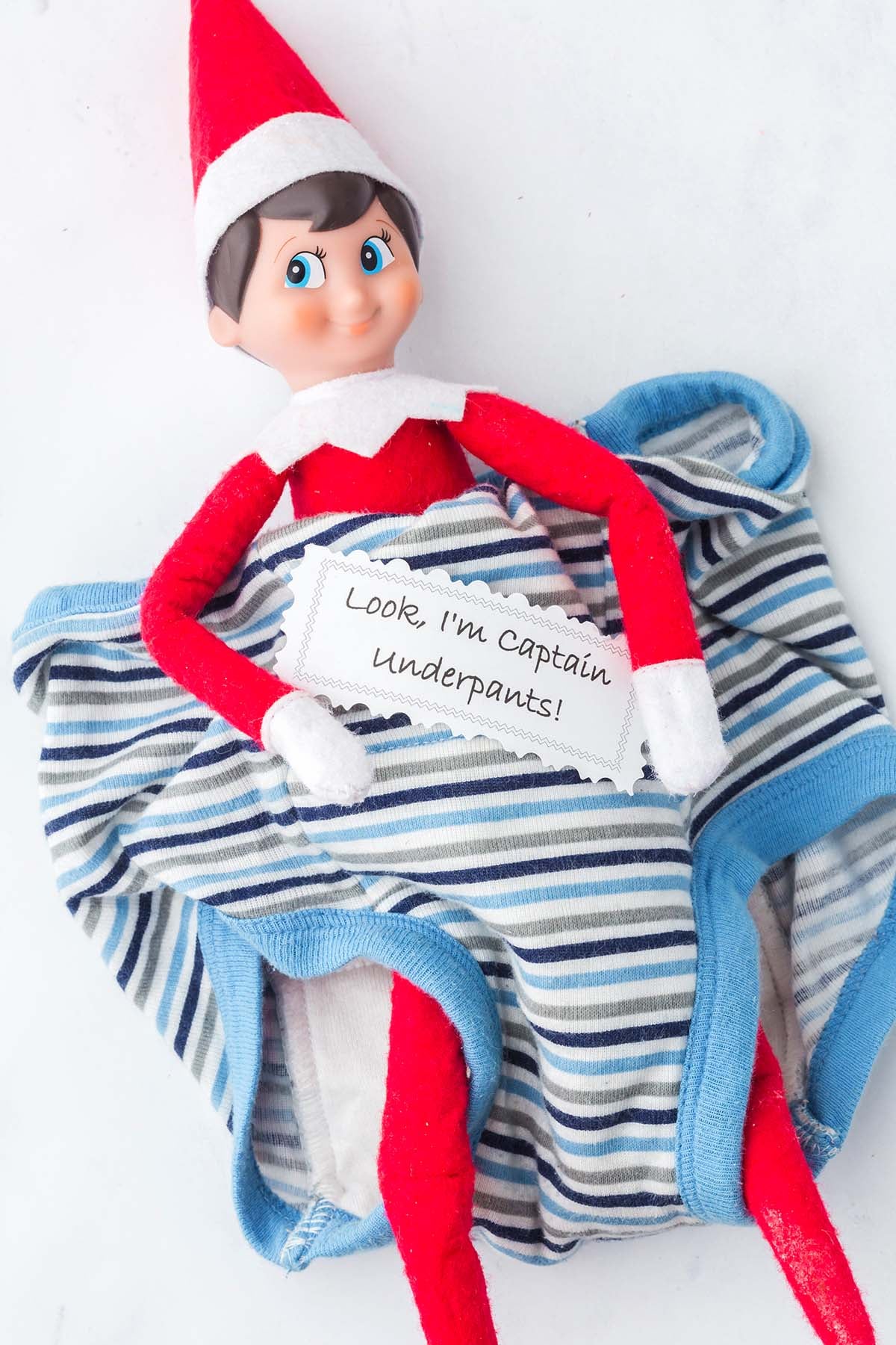 Elf on the Shelf sitting inside striped underwear holding a note that says “Look, I’m Captain underpants!”.