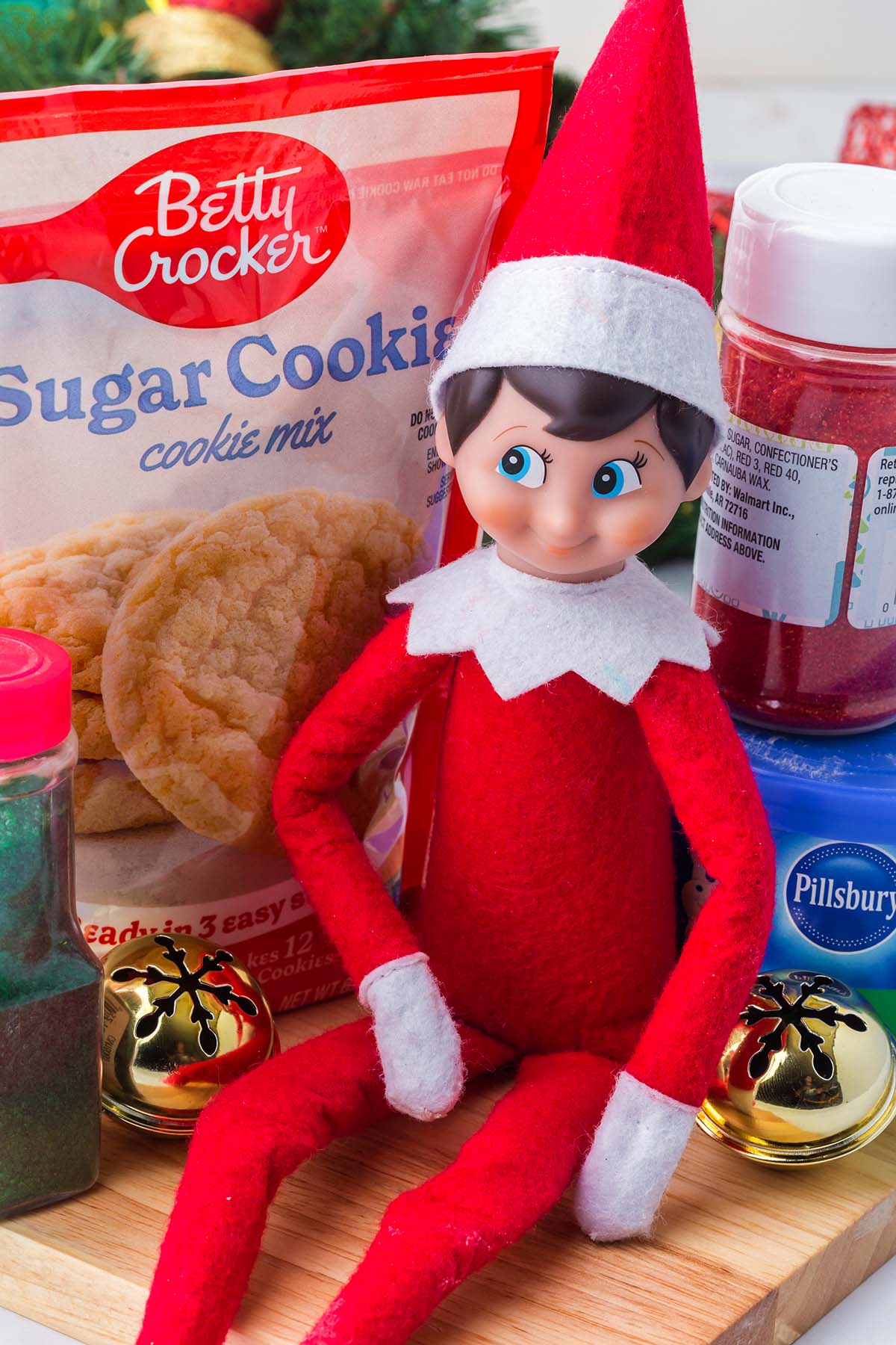 An Elf on the Shelf doll sitting on a wooden board next to a package of Betty Crocker sugar cookie mix.