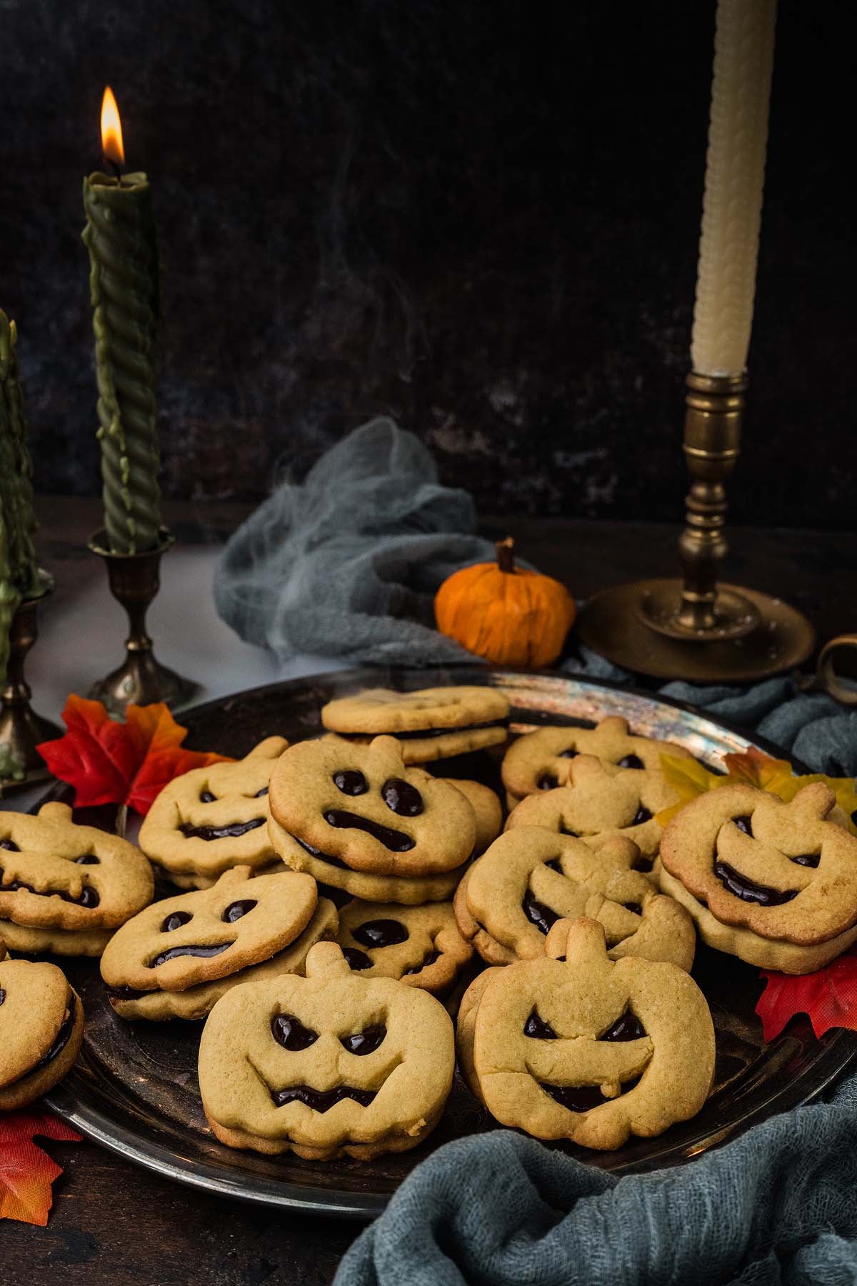 A silver platter piled with pumpkin-shaped sandwich cookies featuring jack-o’-lantern faces.