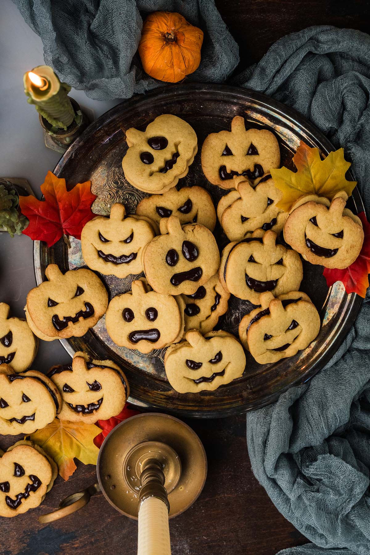A metal platter piled with Jack-o-Lantern pumpkin-shaped sandwich cookies decorated with carved jack-o’-lantern faces.