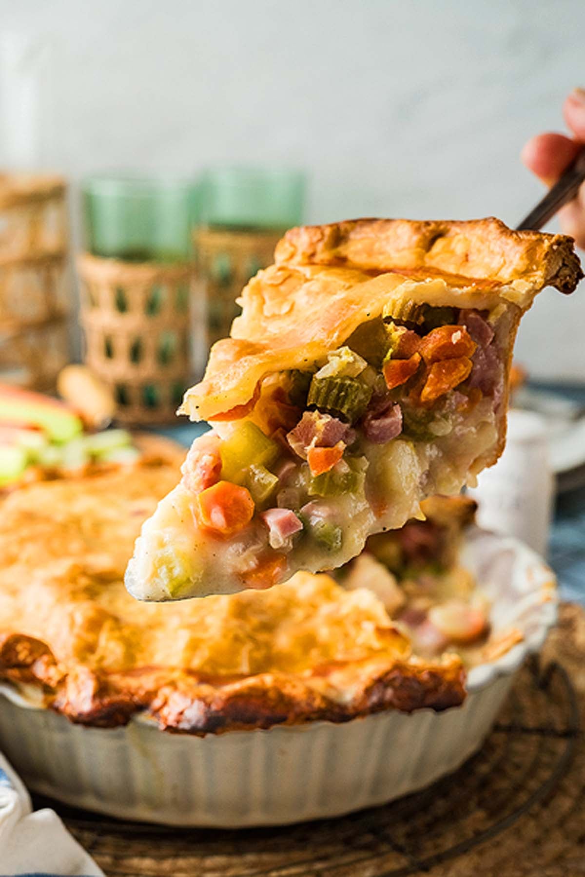 A slice of creamy pot pie filled with ham and vegetables being lifted from a baking dish.