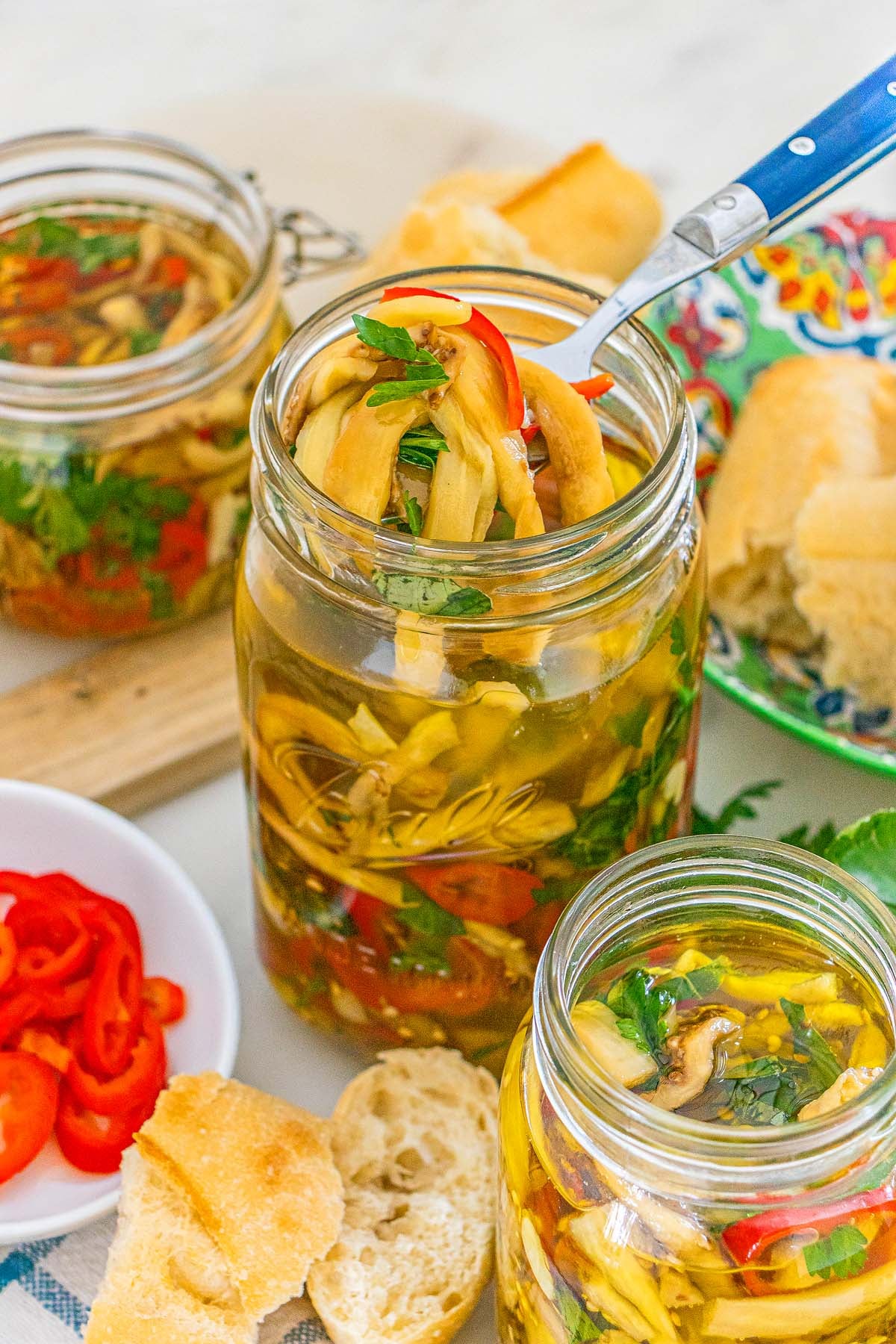 A fork lifting marinated Italian pickled eggplant and sliced red peppers from a glass jar.