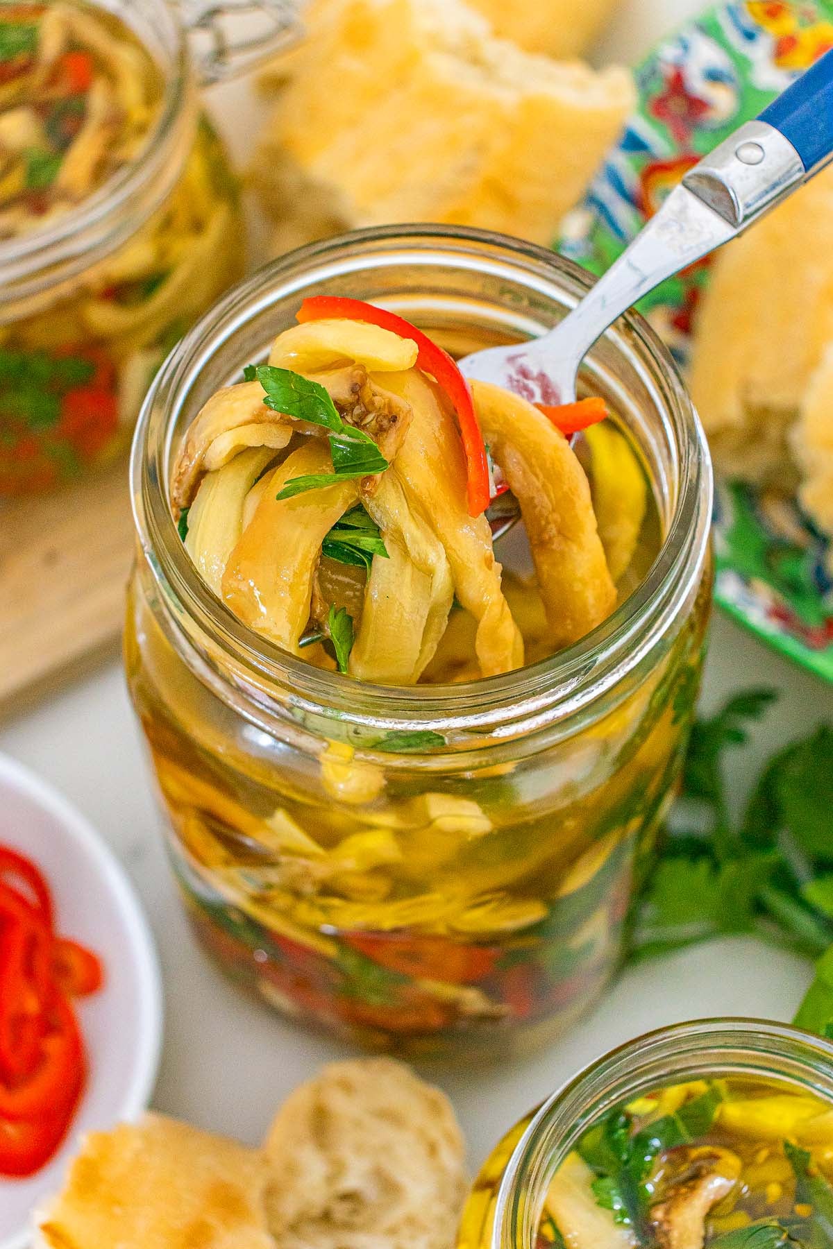 A fork lifts Italian style pickled eggplant from a glass jar.