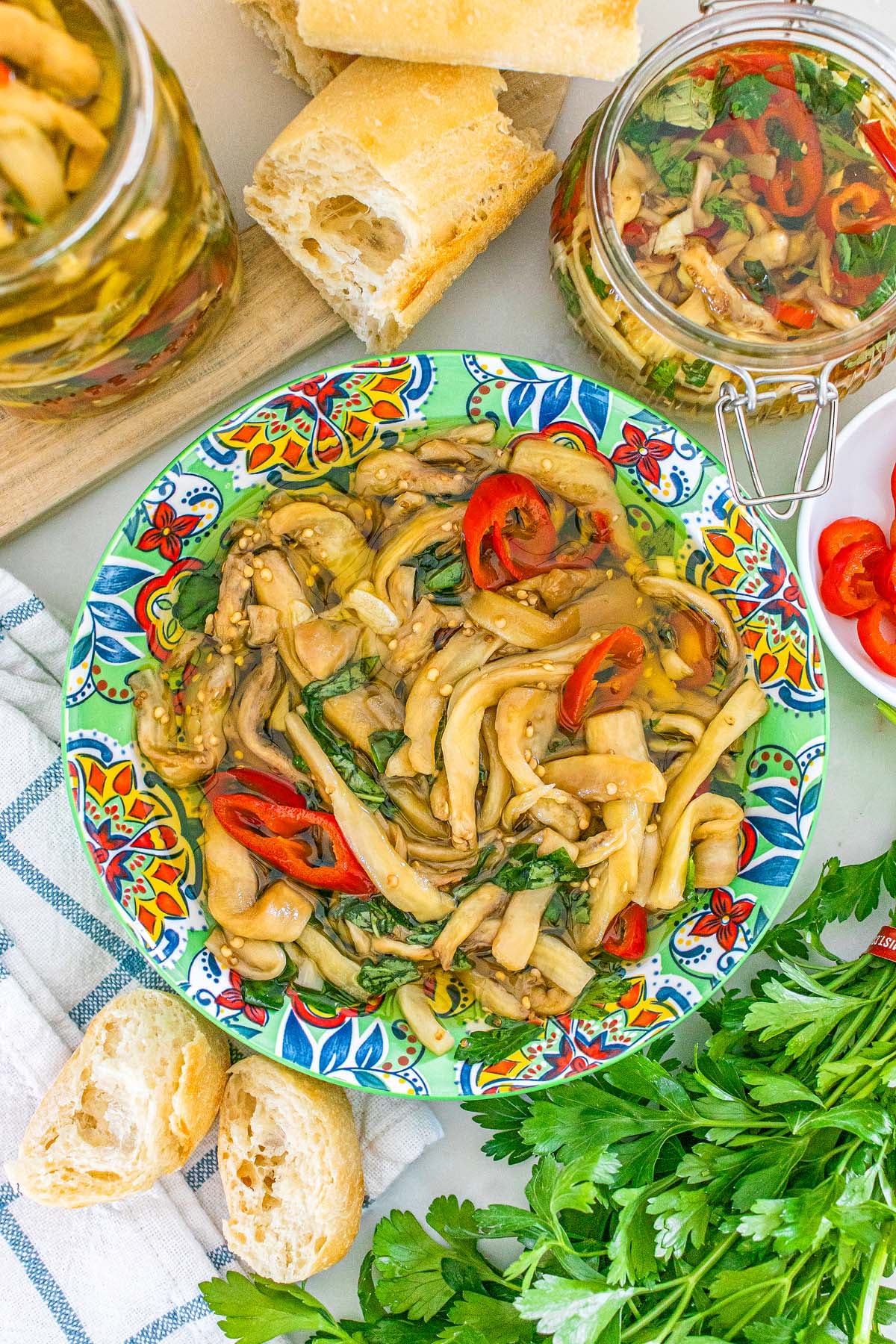 Italian style pickled eggplant on a patterned plate, served with bread and fresh herbs.