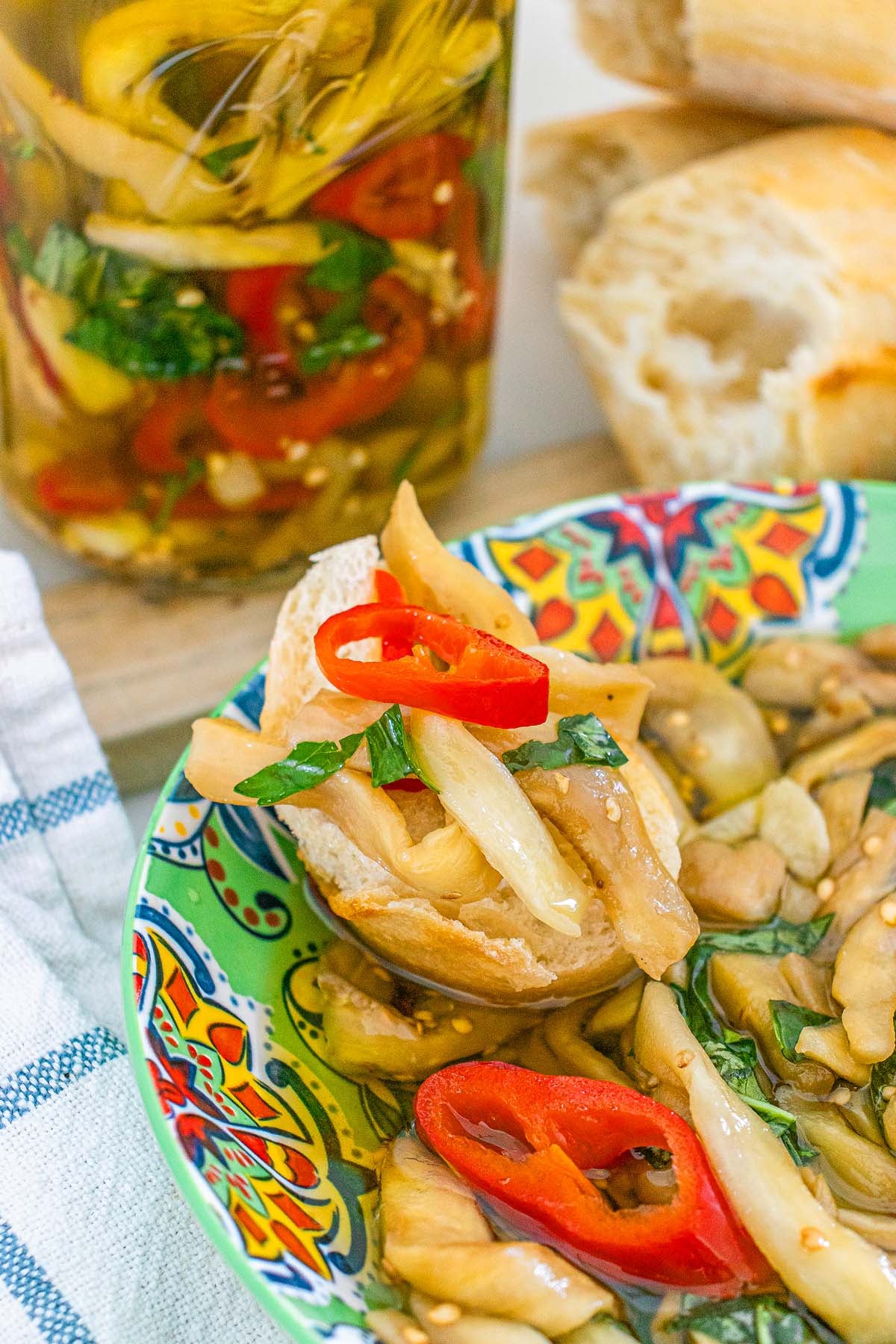 A slice of bread topped with marinated eggplant and sliced red peppers, served in a patterned bowl.