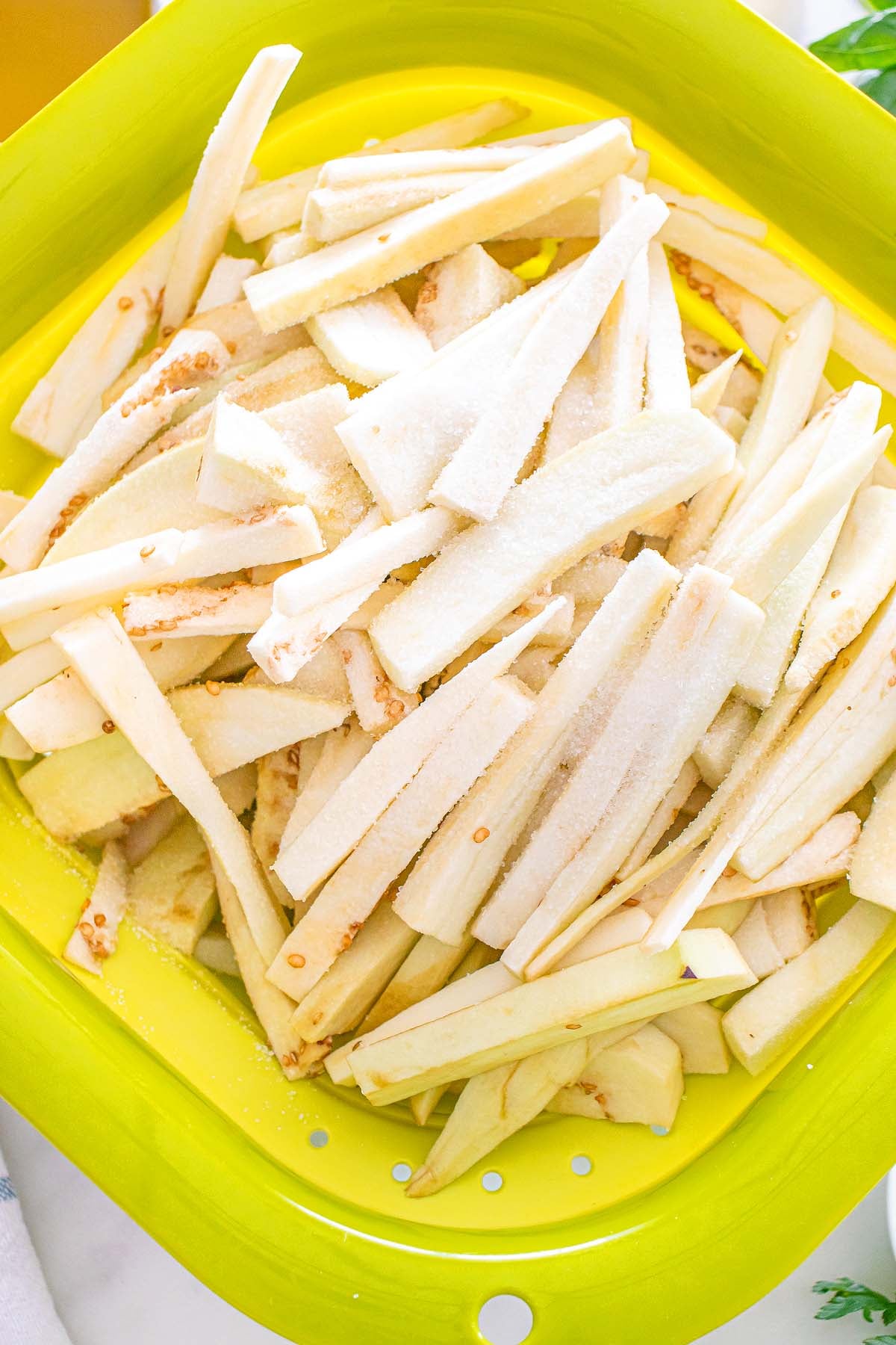 Raw eggplant sticks in a lime green colander.