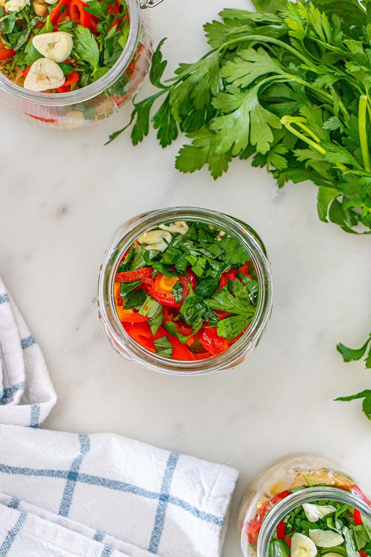 Glass jars filled with sliced red peppers, garlic cloves, and fresh parsley.