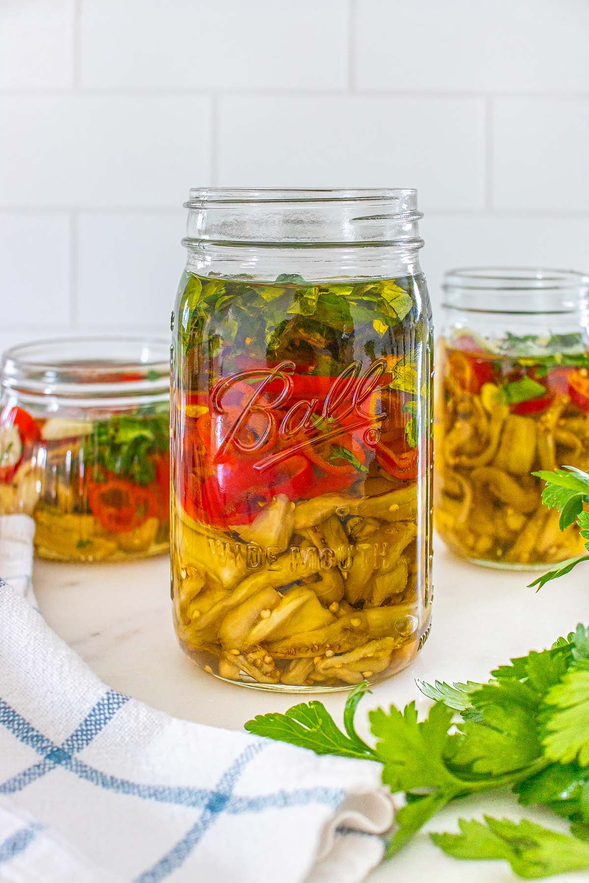 Three glass jars filled with pickled peppers and herbs.