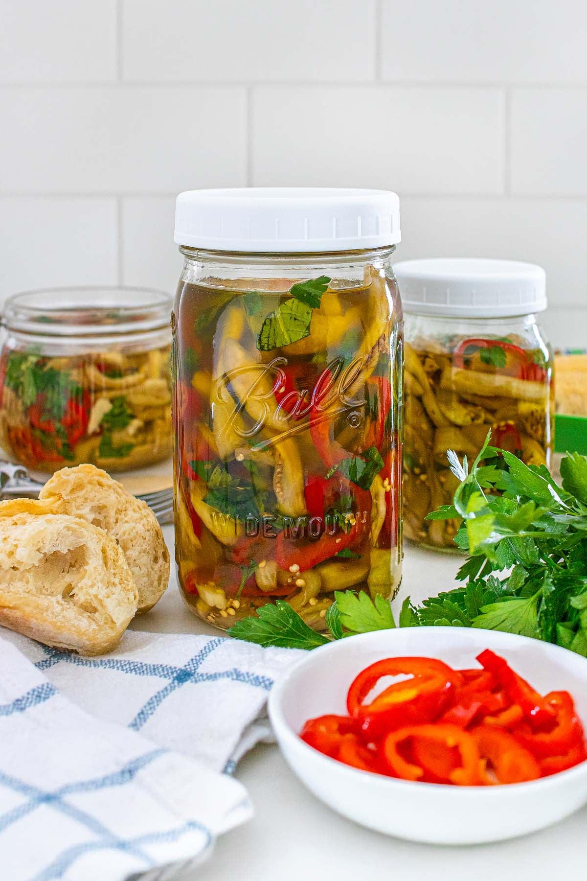 Three glass jars of pickled eggplant, accompanied by crusty bread.