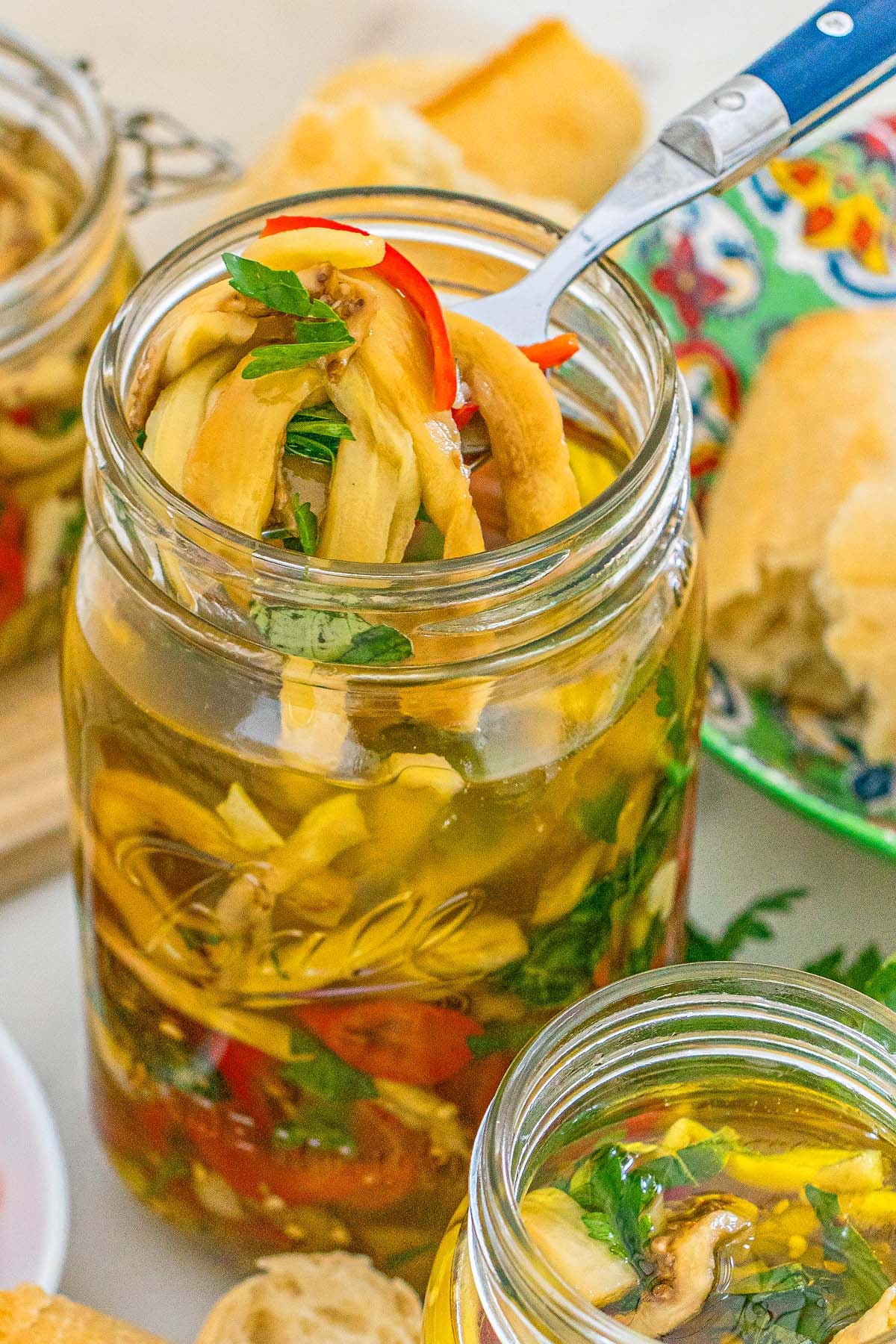 A fork lifts marinated eggplant and red peppers from a glass mason jar.