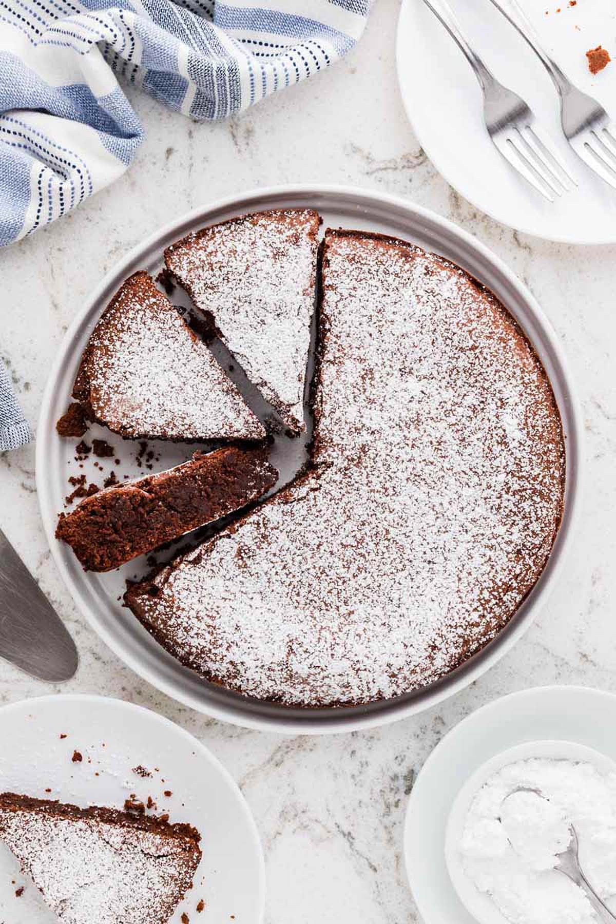 A round Italian flourless chocolate cake dusted with powdered sugar, with two slices cut and served on side plates.