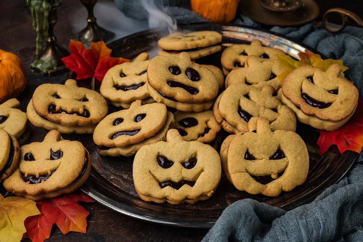 Jack-o-Lantern shaped sandwich cookies with cutout jack-o’-lantern faces on a metal platter.
