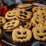 A silver platter piled with Jack-o-Lantern shaped sandwich cookies featuring jack-o’-lantern faces.
