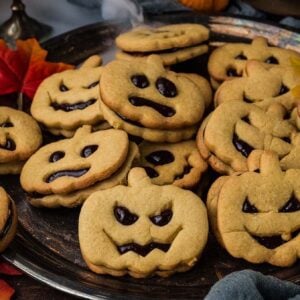 A silver platter piled with Jack-o-Lantern shaped sandwich cookies featuring jack-o’-lantern faces.