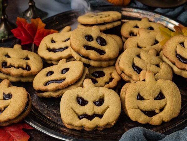 A silver platter piled with Jack-o-Lantern shaped sandwich cookies featuring jack-o’-lantern faces.
