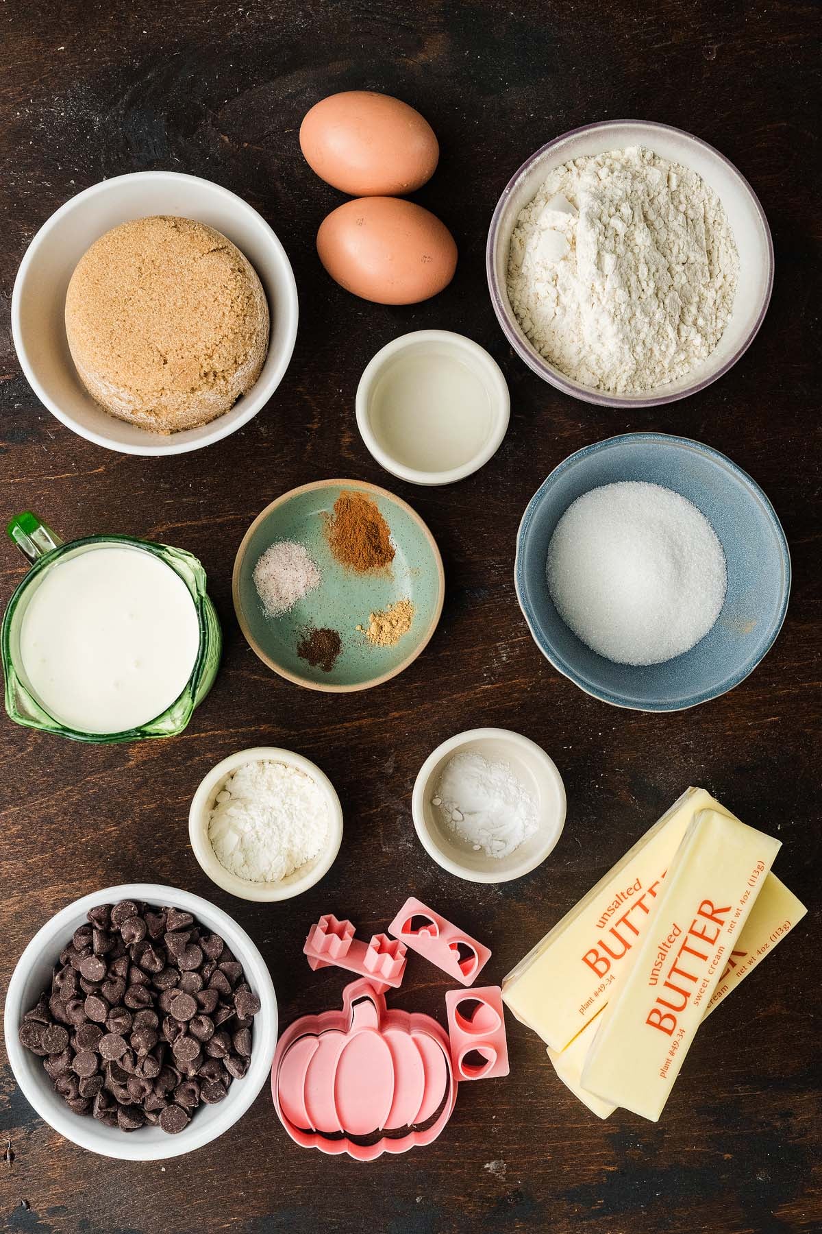 Ingredients for baking including flour, sugar, butter, eggs, chocolate chips, and pumpkin-shaped cookie cutters.