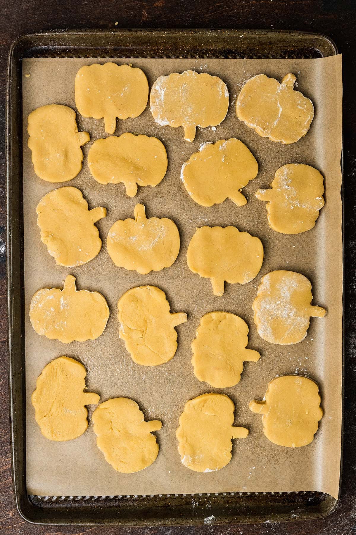 Pumpkin-shaped cookie dough cutouts on a parchment-lined baking sheet.