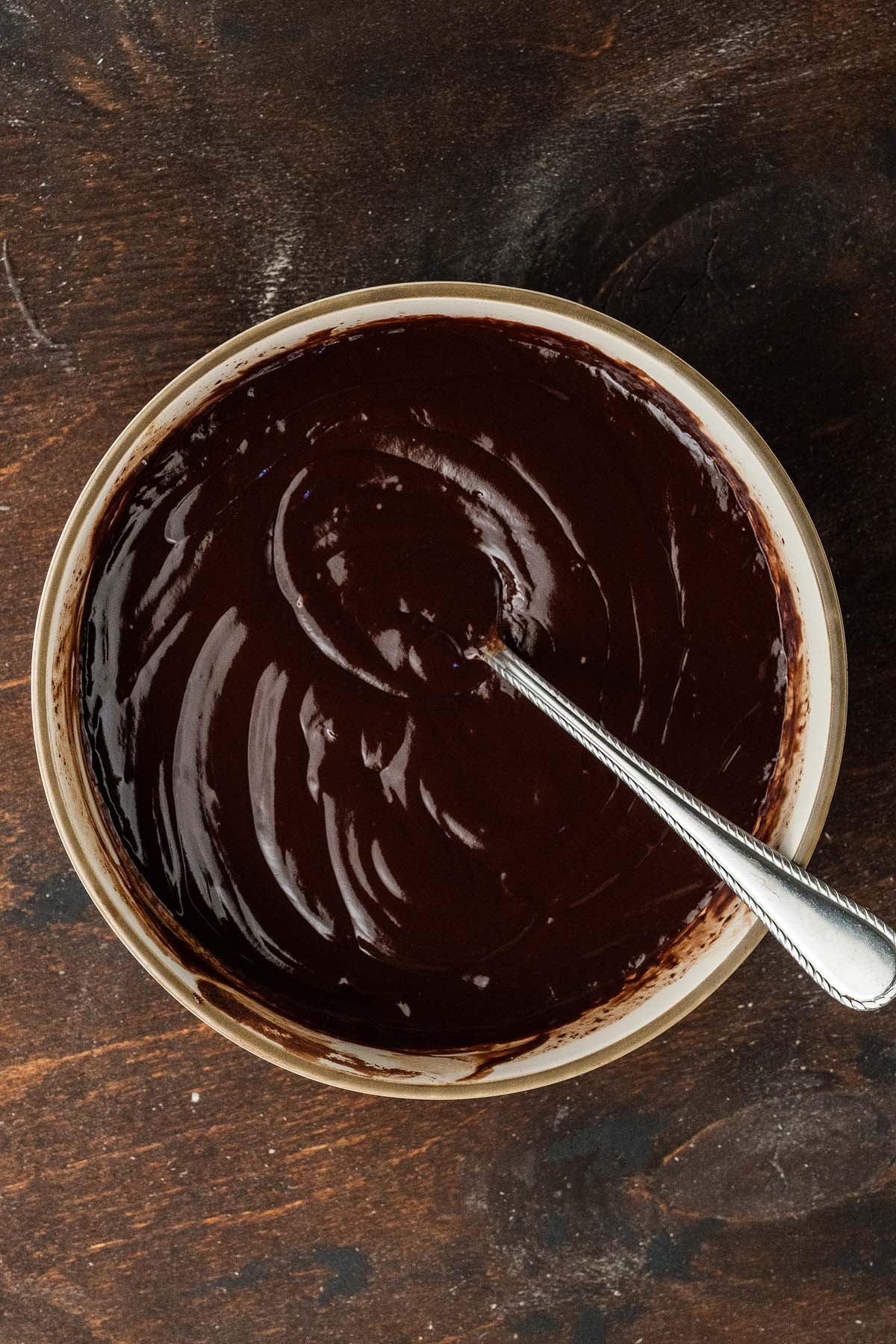 A metal spoon resting in a bowl of dark chocolate ganache.
