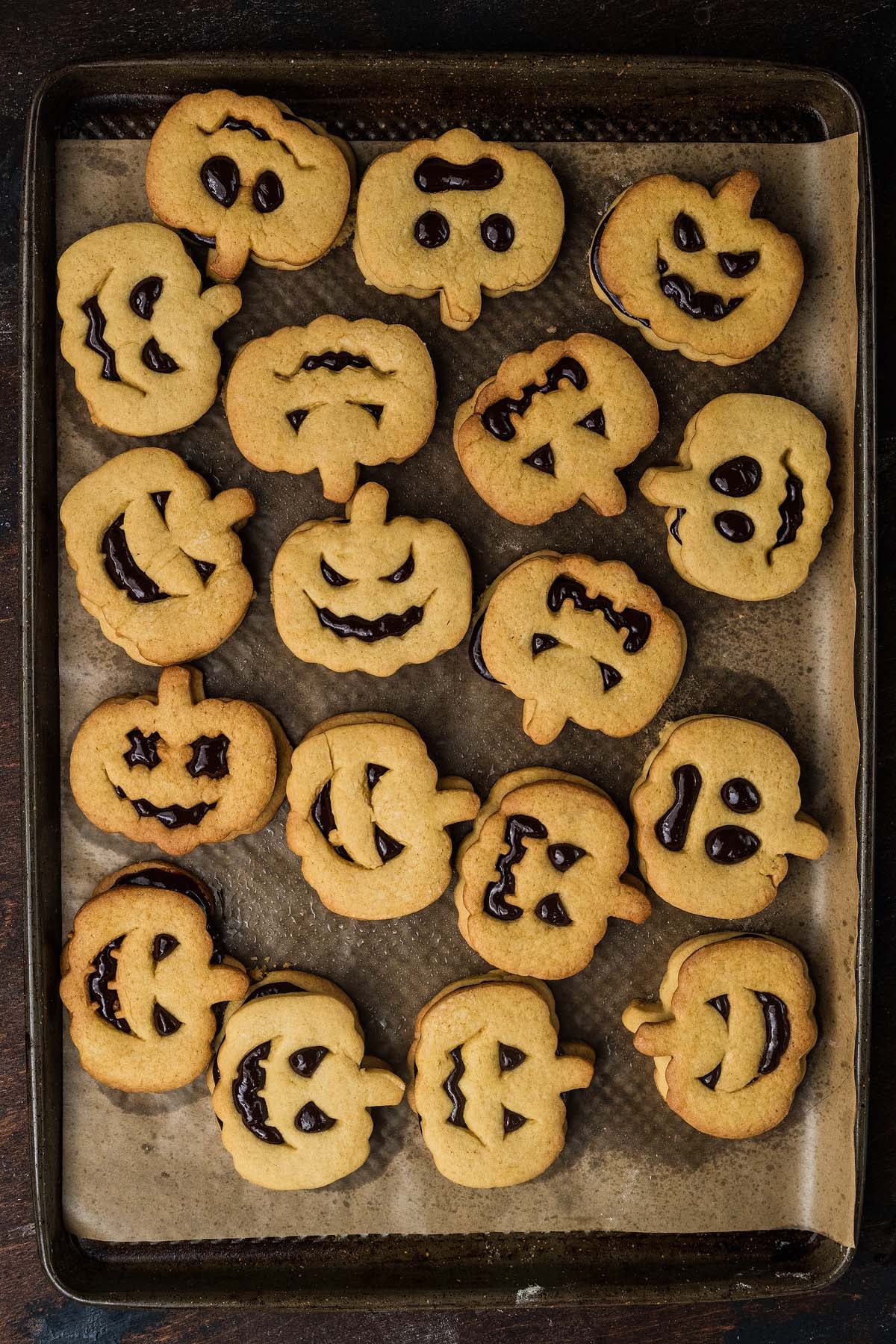 A baking sheet filled with jack-o-lantern shaped sandwich cookies featuring chocolate jack-o’-lantern faces.