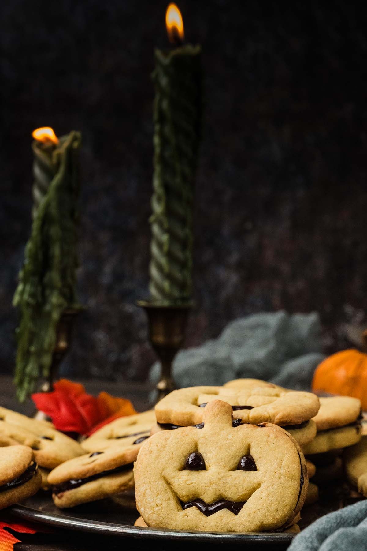 Jack-o’-lantern sandwich cookies filled with dark jam, set before two lit candles.