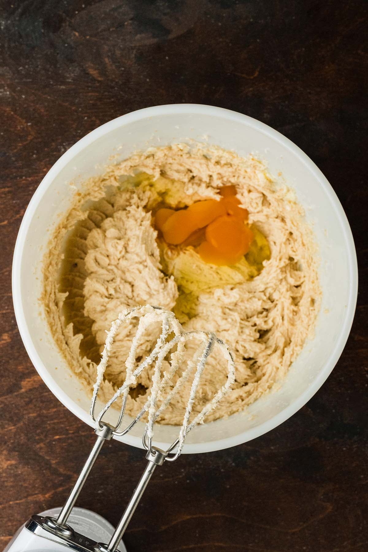 Electric hand mixer beaters in a bowl of cookie dough with raw eggs.