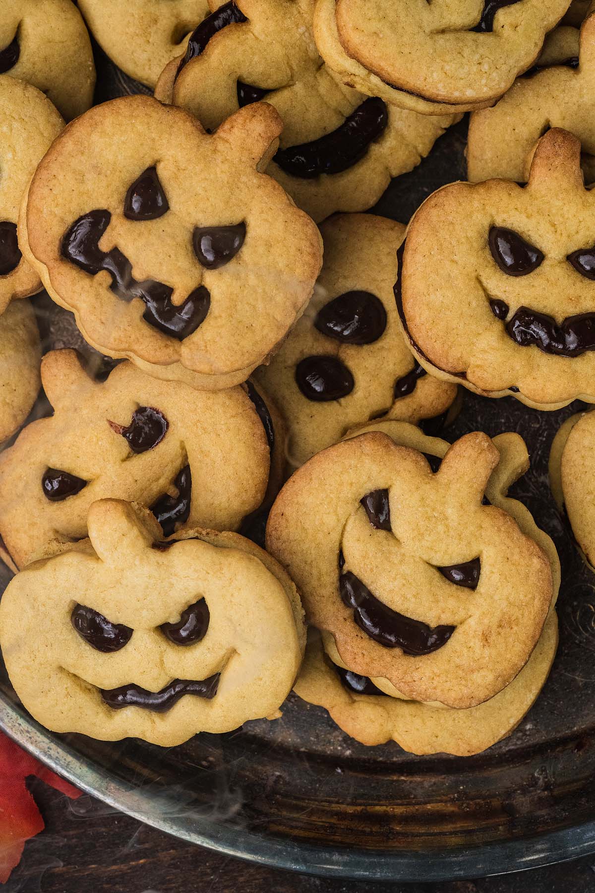 A pile of pumpkin-shaped sandwich cookies filled with dark chocolate.