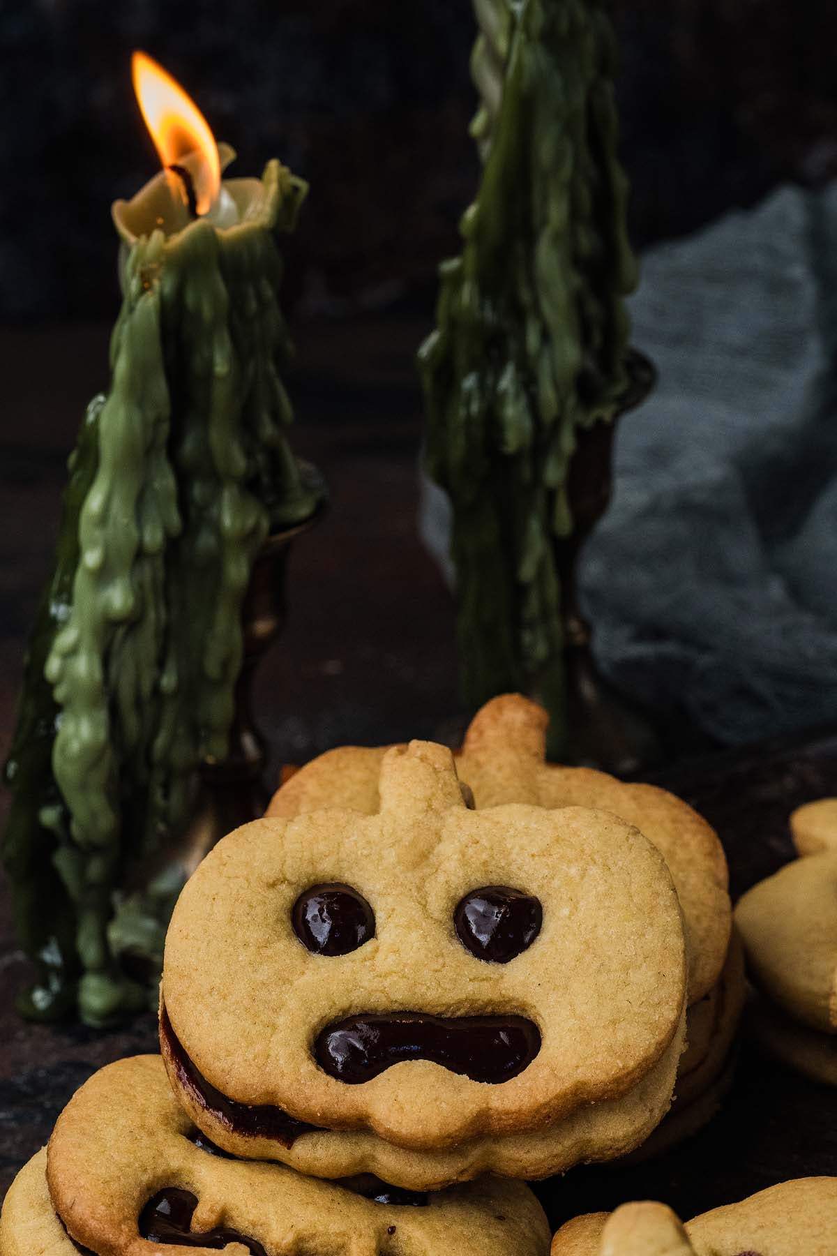 Pumpkin-shaped sandwich cookies with chocolate faces, next to a lit green taper candle.