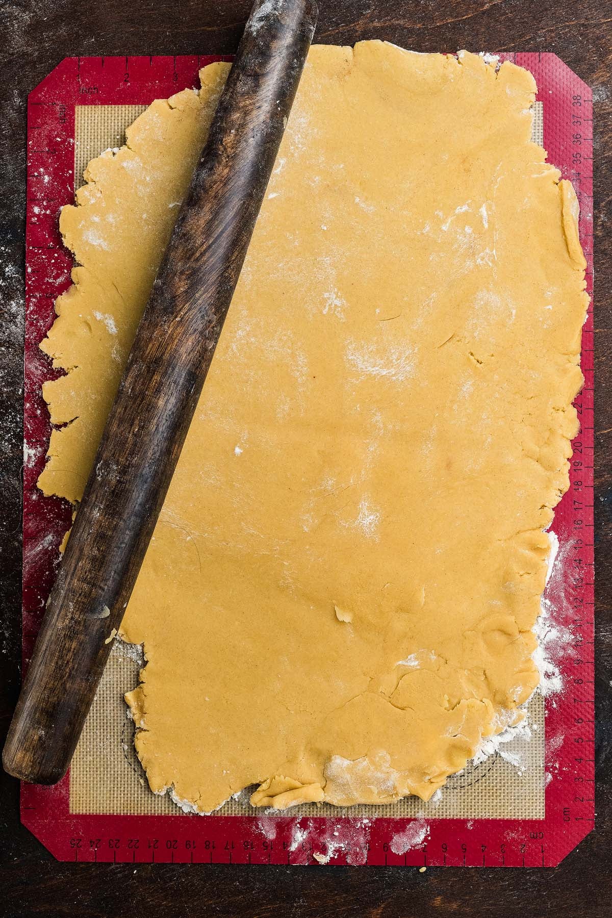 A wooden rolling pin resting on a sheet of rolled-out dough on a silicone baking mat.