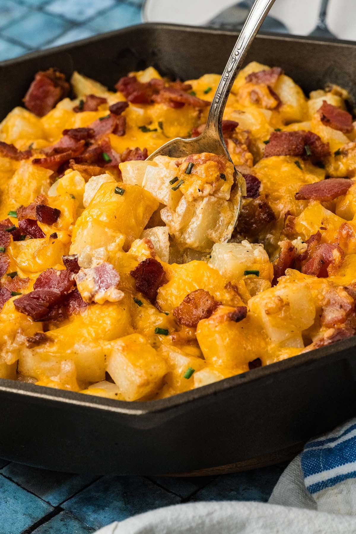 A spoonful of cheesy potatoes topped with bacon and chives in a cast-iron skillet.