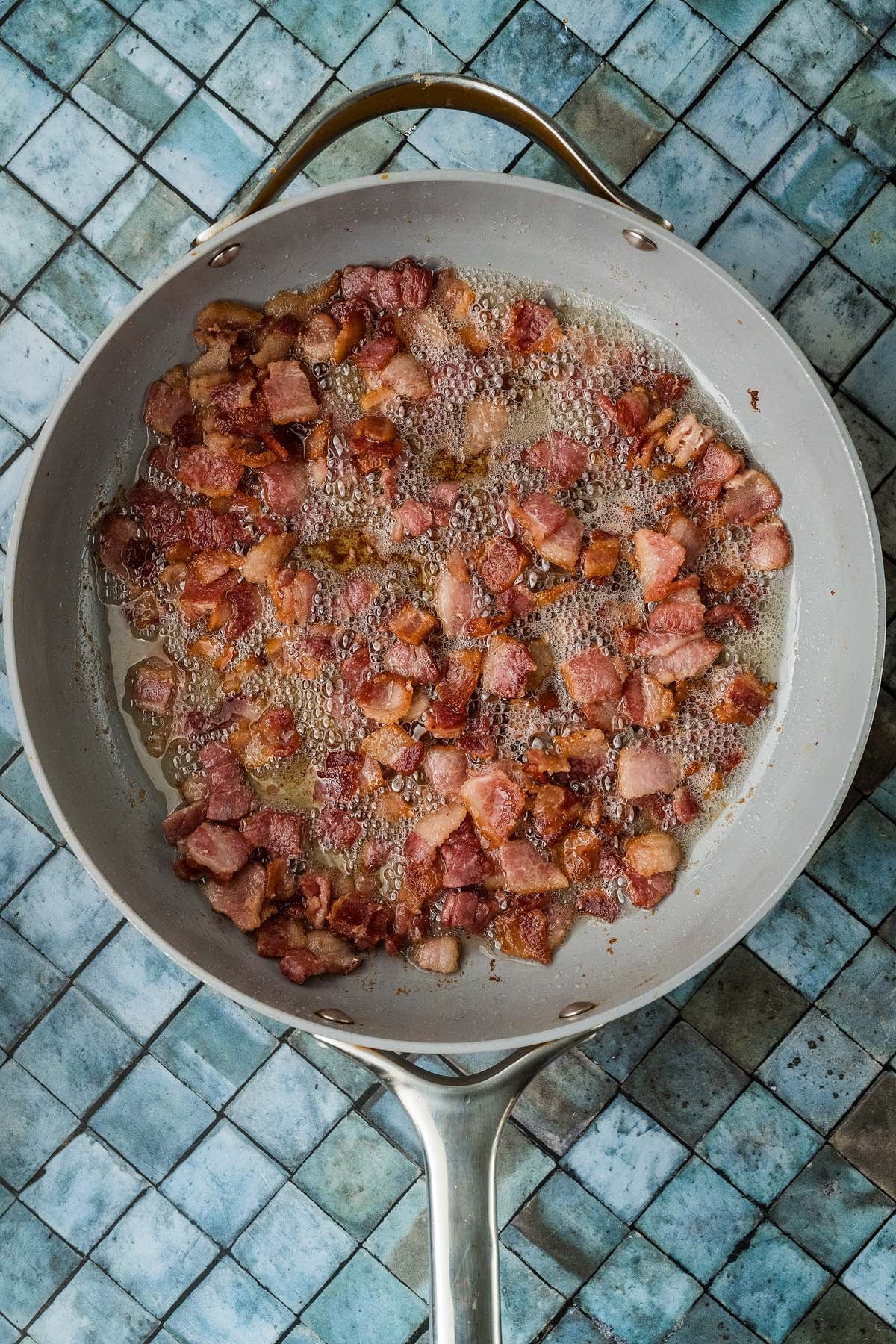 Diced bacon frying in a skillet.