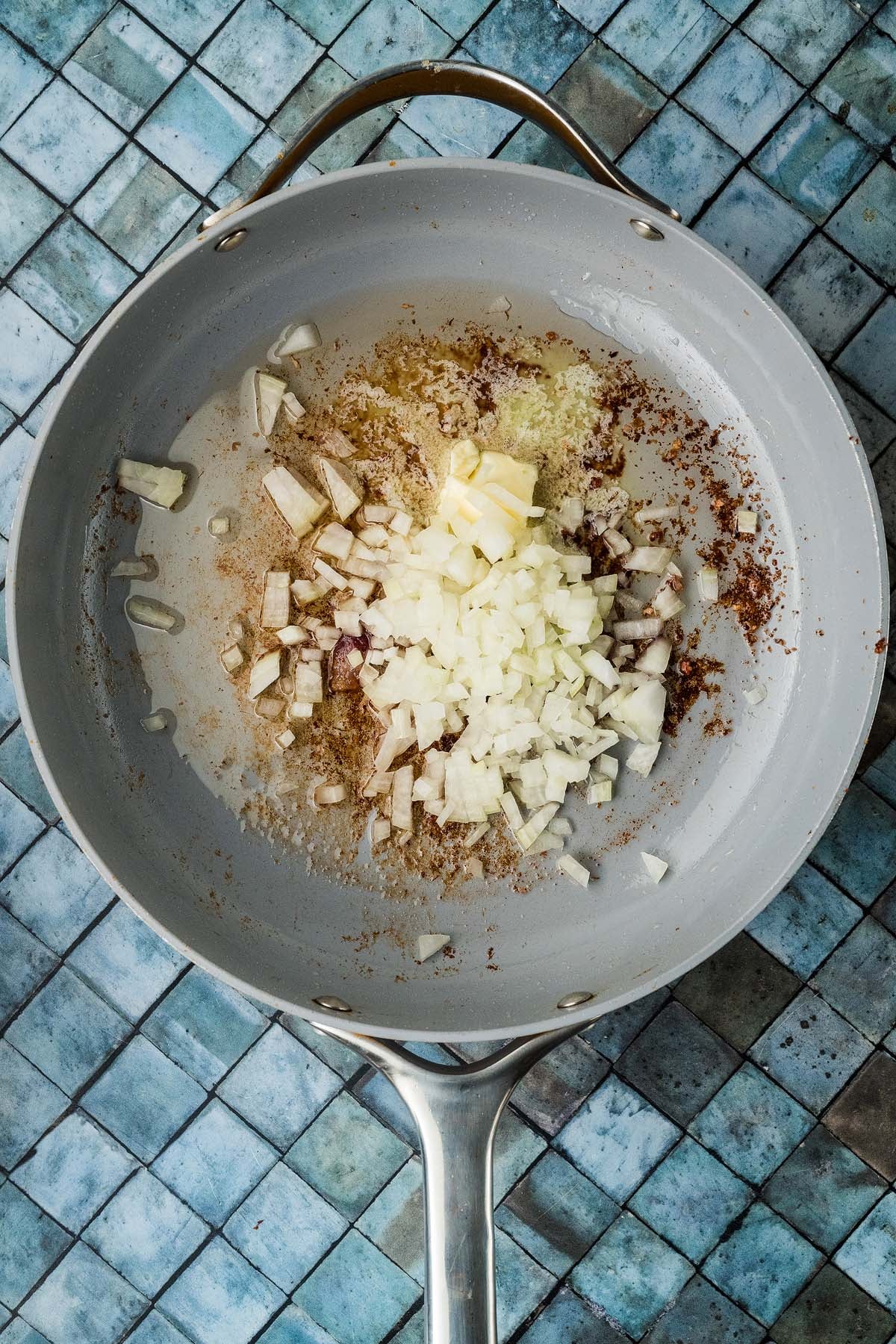 Diced onions and a pat of butter cooking in a nonstick skillet.
