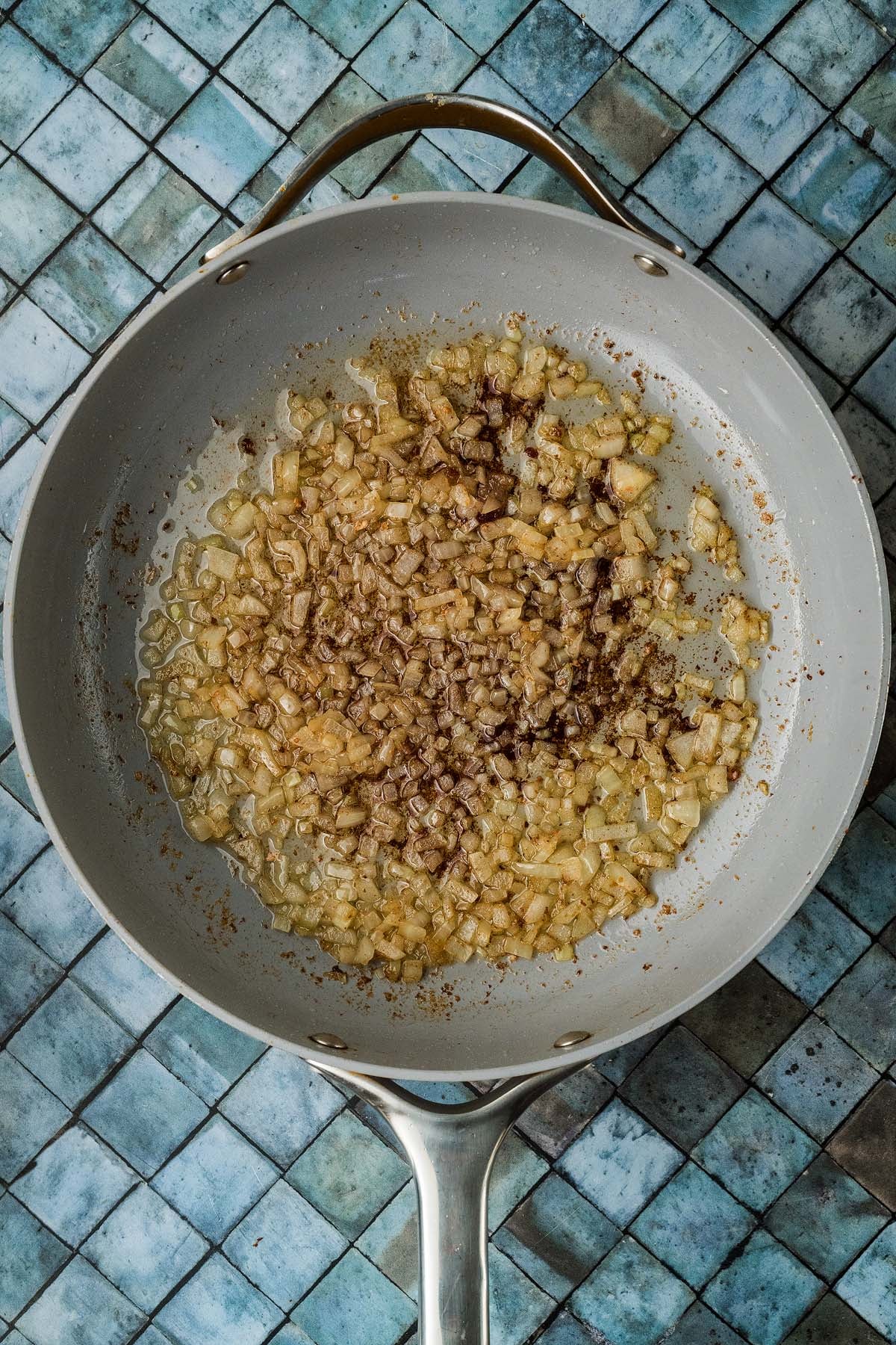 Diced onions sautéing in a grey skillet.