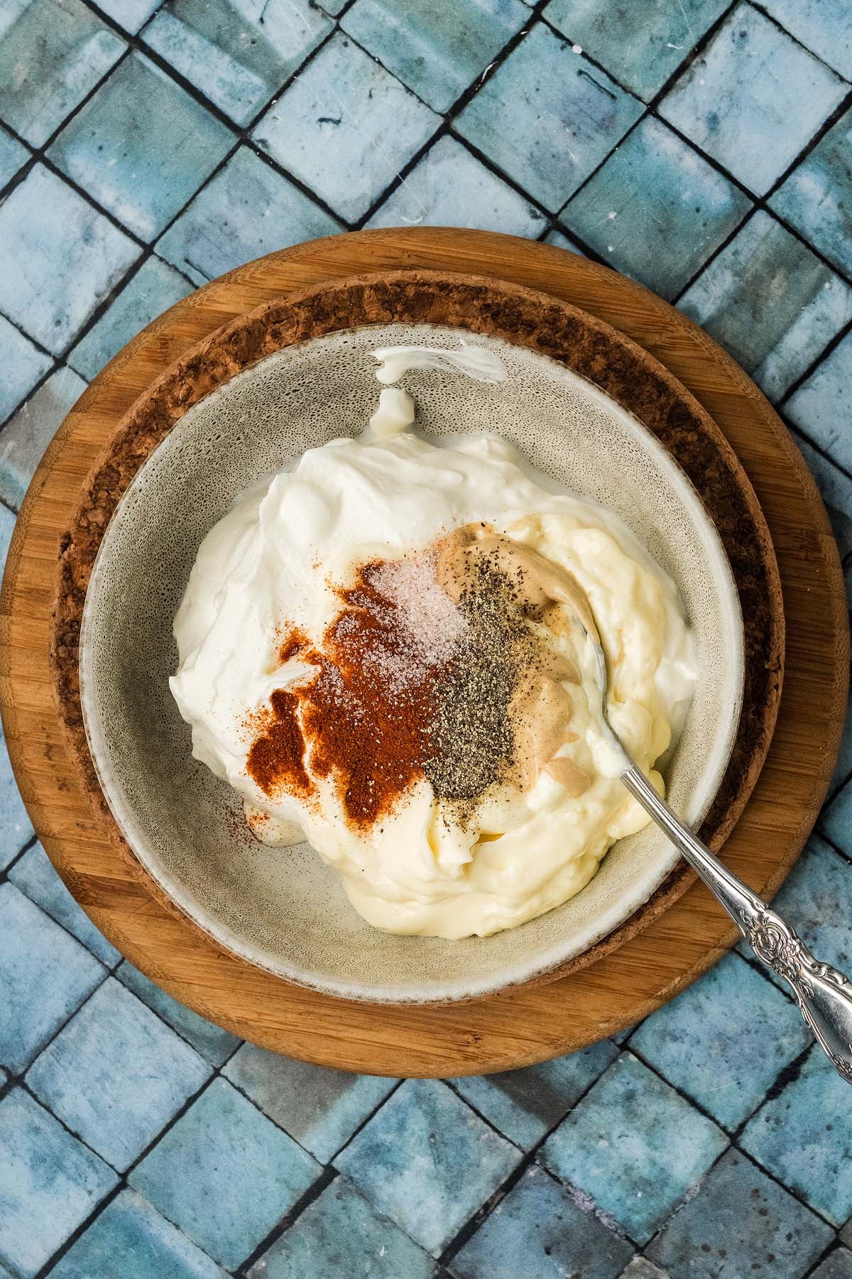 A bowl of mayonnaise and sour cream topped with spices and a spoon.