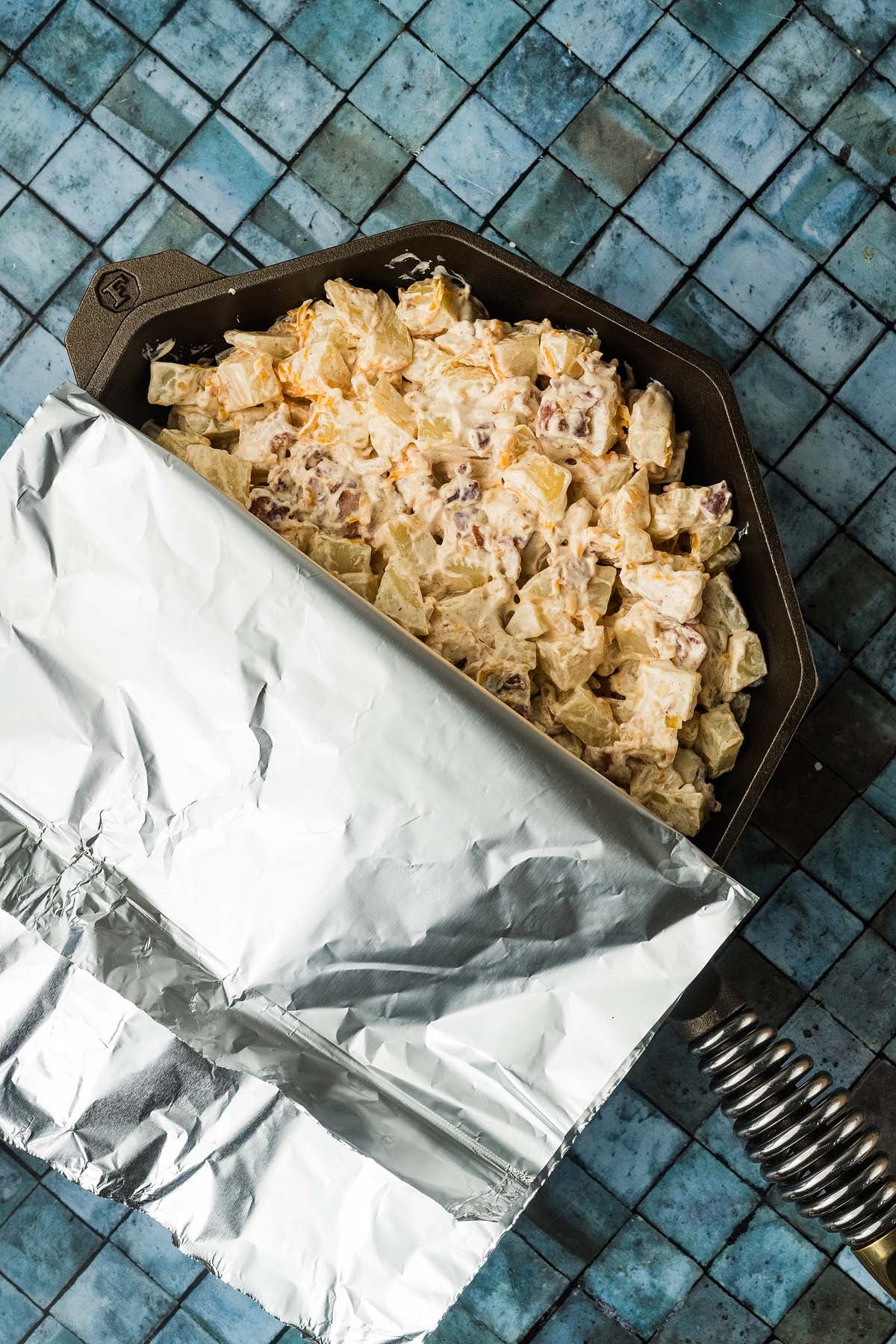 Mississippi mud potatoes in a cast-iron skillet, partially covered with aluminum foil.