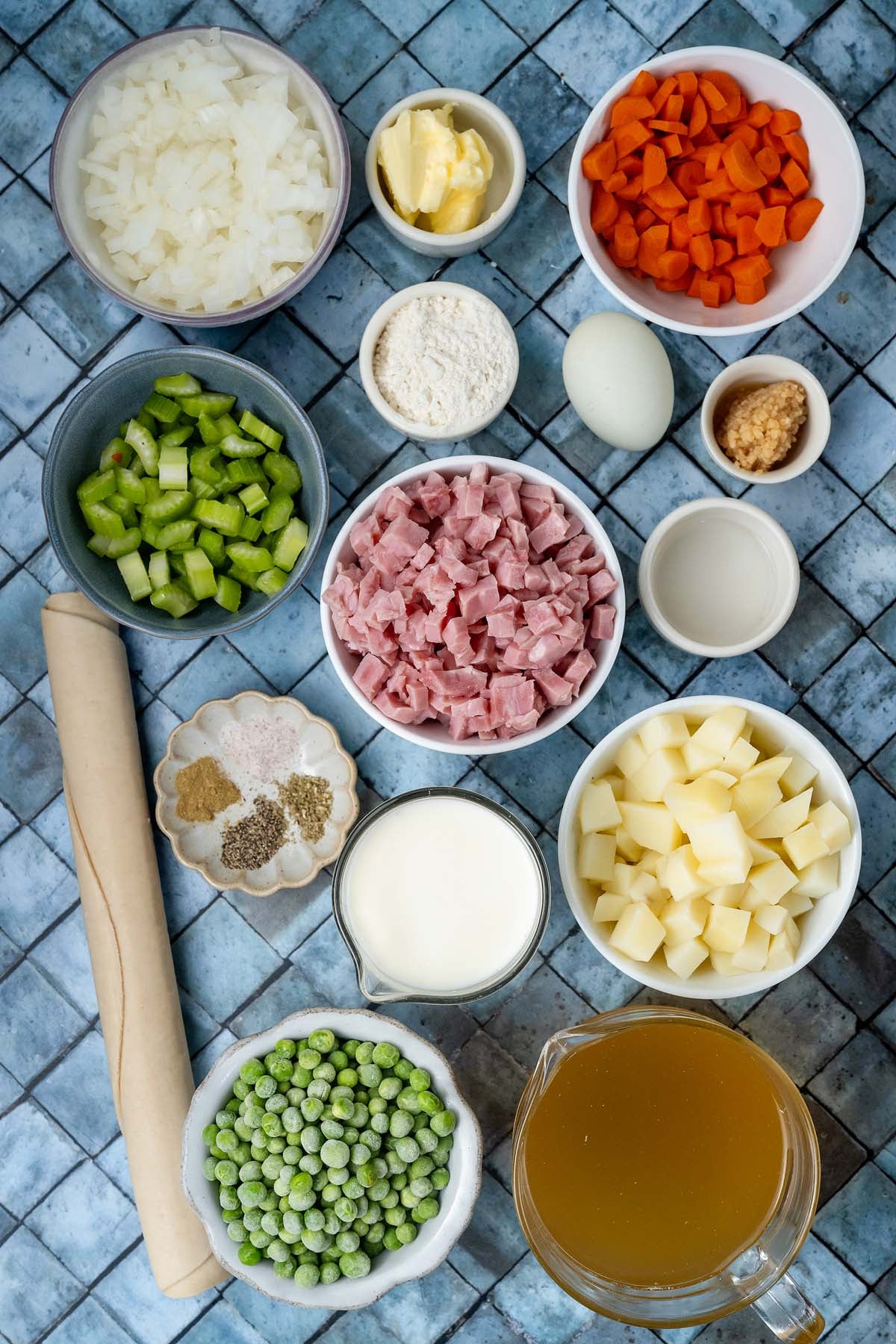 Ingredients for pot pie in small bowls, including diced ham, vegetables, broth, and a rolled pastry crust.