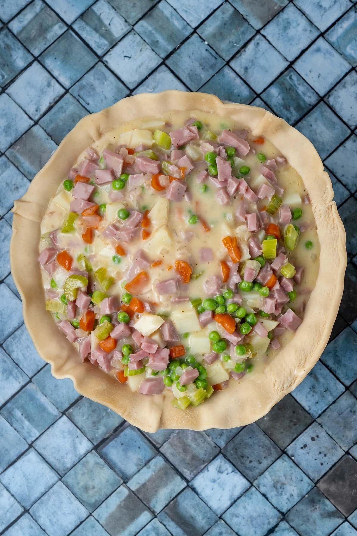 Unbaked pot pie filling with ham, peas, carrots, and potatoes in a crimped pastry crust.