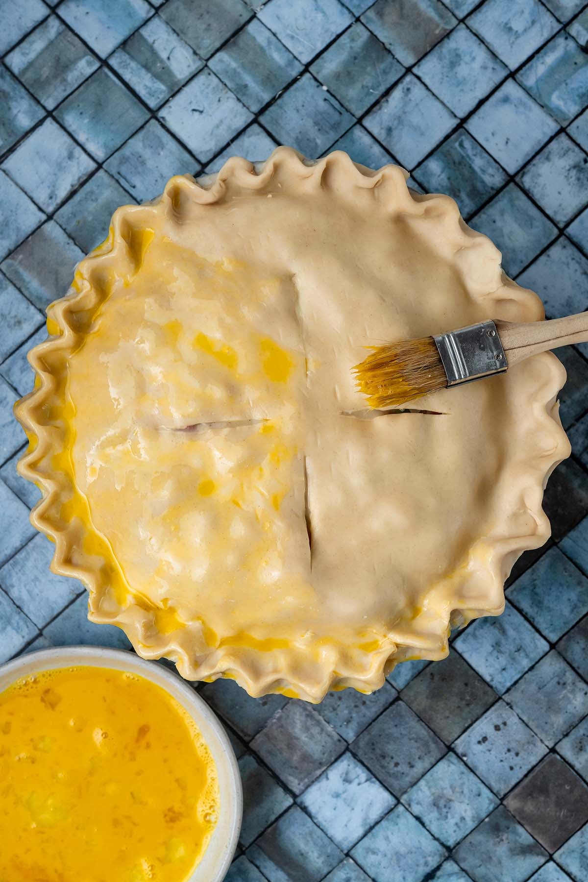 A pastry brush applying egg wash to an unbaked pie crust.