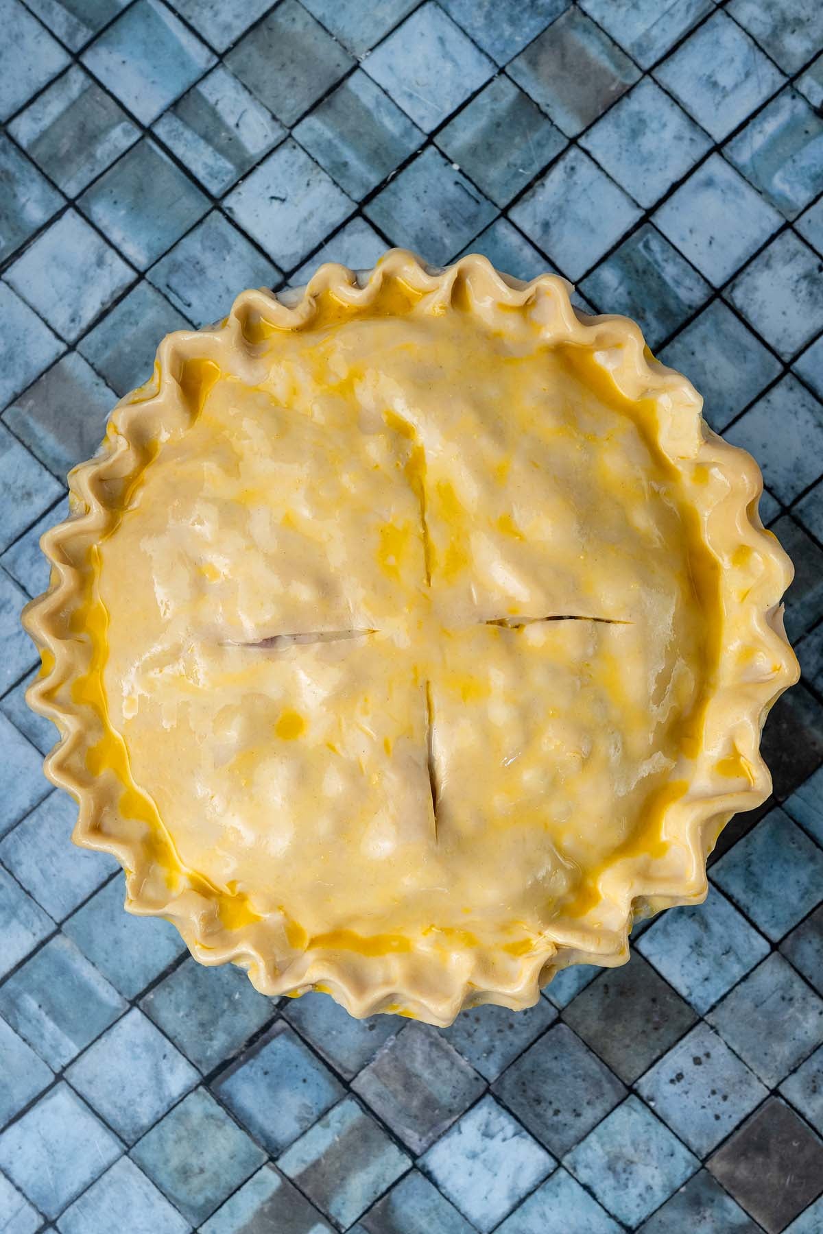 Unbaked pie with a fluted crust and egg wash, viewed from directly above.